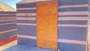 A small, single-room tent with a wooden door and striped fabric walls.