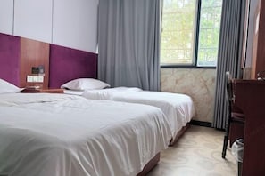 Ein Hotelzimmer mit zwei Betten, einem Holzkopfteil, einem Fenster mit Vorhängen und einem Schreibtisch mit Stuhl.
