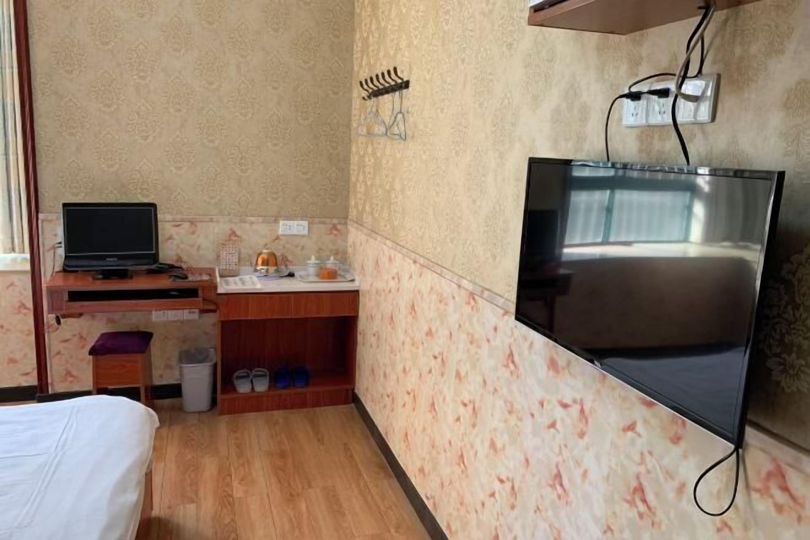 A hotel room with a bed, a desk with a laptop, a TV, and a small kitchenette area.