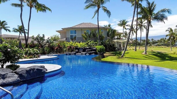 Una piscina con una casa al fondo, rodeada de palmeras.