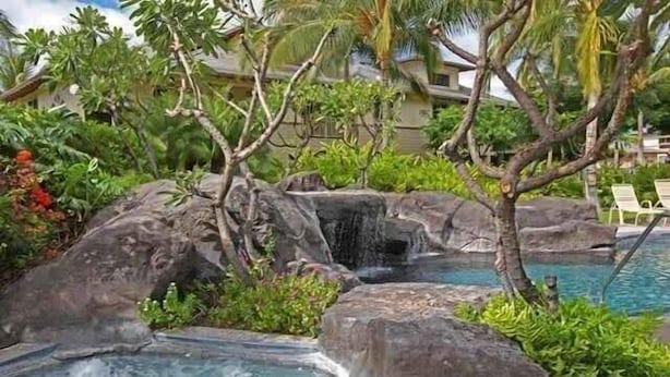 A tropical resort pool area with a waterfall, lush greenery, and lounge chairs. - Mauna Lani Beach club access, Pool & BBQ area (Kamuela)
