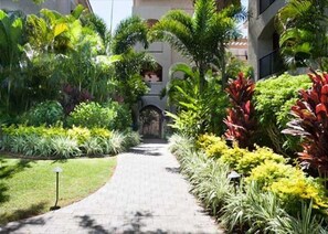 Un chemin menant à l’entrée d’un bâtiment, lequel est entouré d’une végétation luxuriante et d’un jardin bien entretenu.