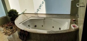 Un bain à remous installé dans un coin, avec un sol carrelé, une petite plante et un porte-serviettes.