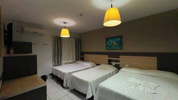Habitación de hotel con tres camas, un televisor de pantalla plana, aire acondicionado y un cuadro en la pared.