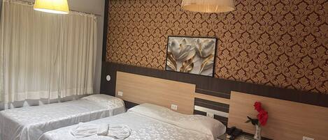 Une chambre d’hôtel avec deux lits simples, une table de chevet avec une lampe, un téléphone et un panneau décoratif mural.