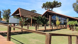 Une structure en bois avec une passerelle couverte menant à un bâtiment doté de grandes fenêtres et d’un arbre devant.