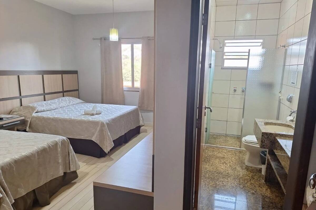 A hotel room with two beds, a bathroom with a sink and toilet, and a view of the outdoors through a window.
