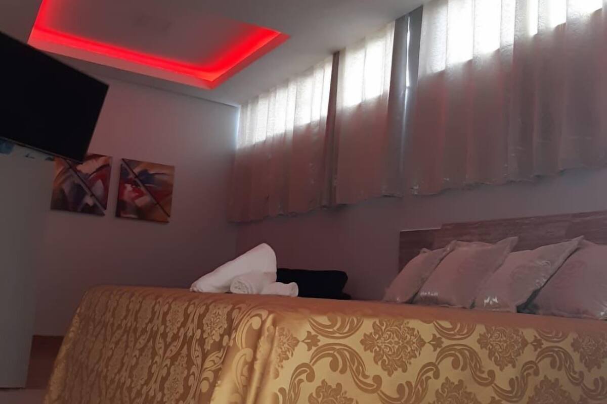 A bedroom with a bed, a flat-screen TV, and a ceiling with red lighting.