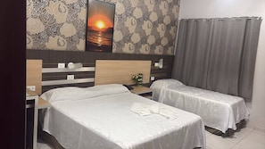 Hotellihuone, jossa on kaksi erillistä sänkyä, puinen pääty, yöpöytä lampun kanssa ja seinälle ripustettu maalaus, jossa on kuvattuna auringonlasku.