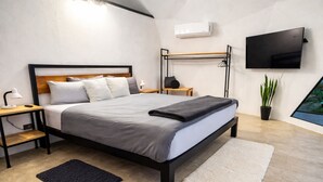 Une chambre à coucher moderne avec un lit, des tables de chevet, une télévision, une plante et une fenêtre.