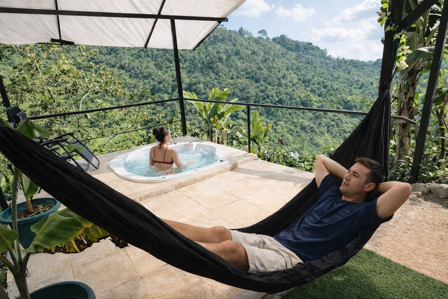 Una hamaca, un jacuzzi y vistas a una montaña verde y exuberante.