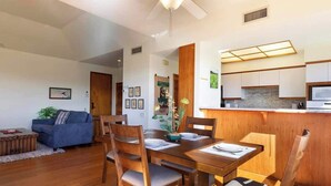 Una sala de estar moderna con una mesa de comedor preparada para cuatro personas, sillas de madera, un sofá azul y una cocina con armarios de madera y una encimera.