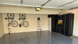 Un garage avec un sol en béton poli, des vélos fixés au mur, une échelle et des armoires de rangement.