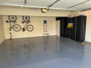 Un garaje con piso de concreto pulido, bicicletas colgadas en la pared, una escalera y armarios de almacenamiento.