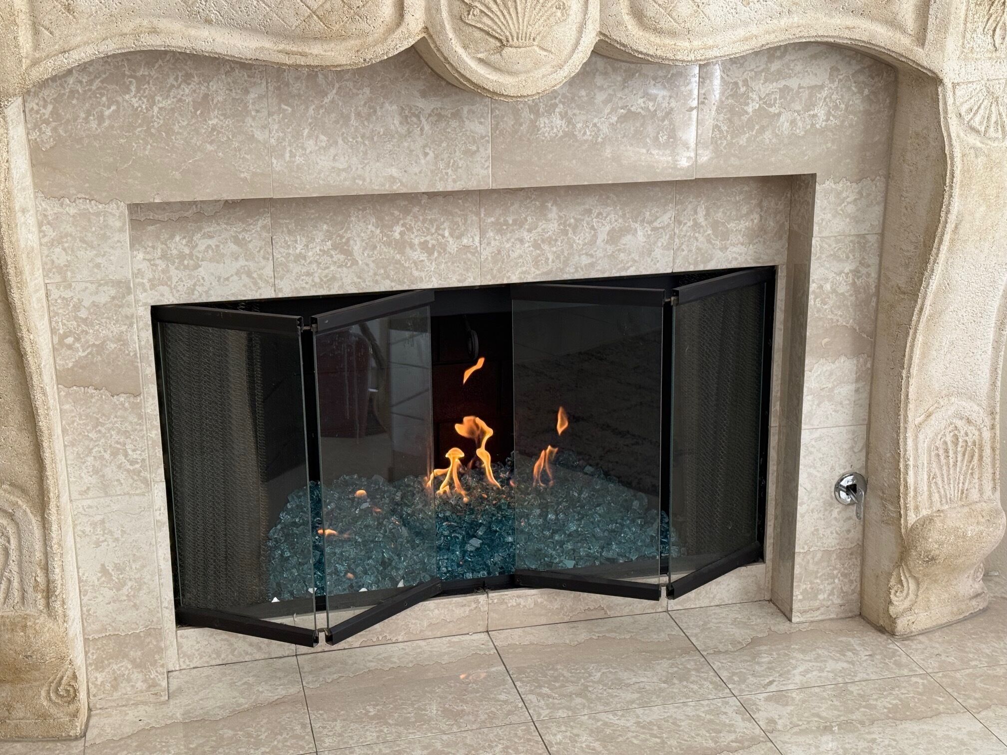 Ein moderner Kamin mit Glasscheibe, brennenden Holzscheiten und aufwendiger Steinmetarbeit.