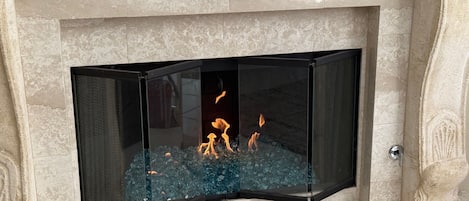 A modern fireplace with a glass screen, burning logs, and ornate stonework.
