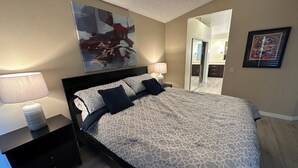 Une chambre à coucher avec un lit, une table de chevet, une lampe, un tableau et un miroir.