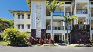 A multi-story hotel with a symmetrical facade, balconies, and a landscaped entrance. - Beach club access, pool, Complex on A-bay, Private (Waikoloa Village)
