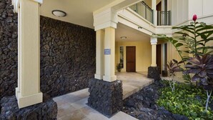 A stone-clad entrance with a beige pillar, a balcony, and a sign indicating a room number. - Beach club access, pool, Complex on A-bay, Private (Waikoloa Village)