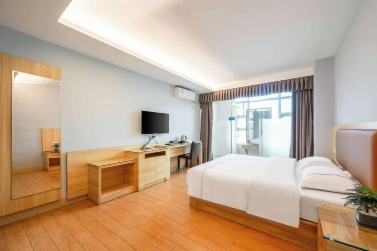 Ein Hotelzimmer mit Bett, Schreibtisch, Stuhl, Fernseher und einem großen Fenster.