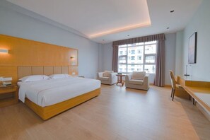 A hotel room with a large bed, a desk, a chair, and a window with curtains.
