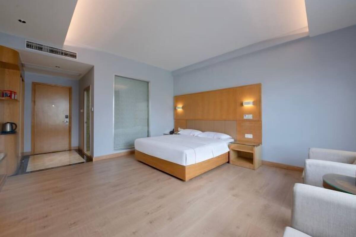 Ein modernes Hotelzimmer mit einem hölzernen Bett, Nachttischen, einer kleinen Sitzecke und einer Tür zu einem Badezimmer.