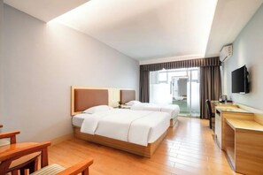 A hotel room with two beds, a desk, a chair, and a TV.
