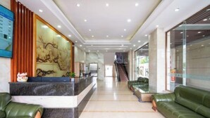 A hotel lobby with a reception desk, green leather sofas, a staircase, and a large wall mural. - Yangjiang Jinrui Business Hotel (Yangjiang)