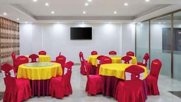 A conference room with round tables, red chairs, and a flat-screen TV on the wall.