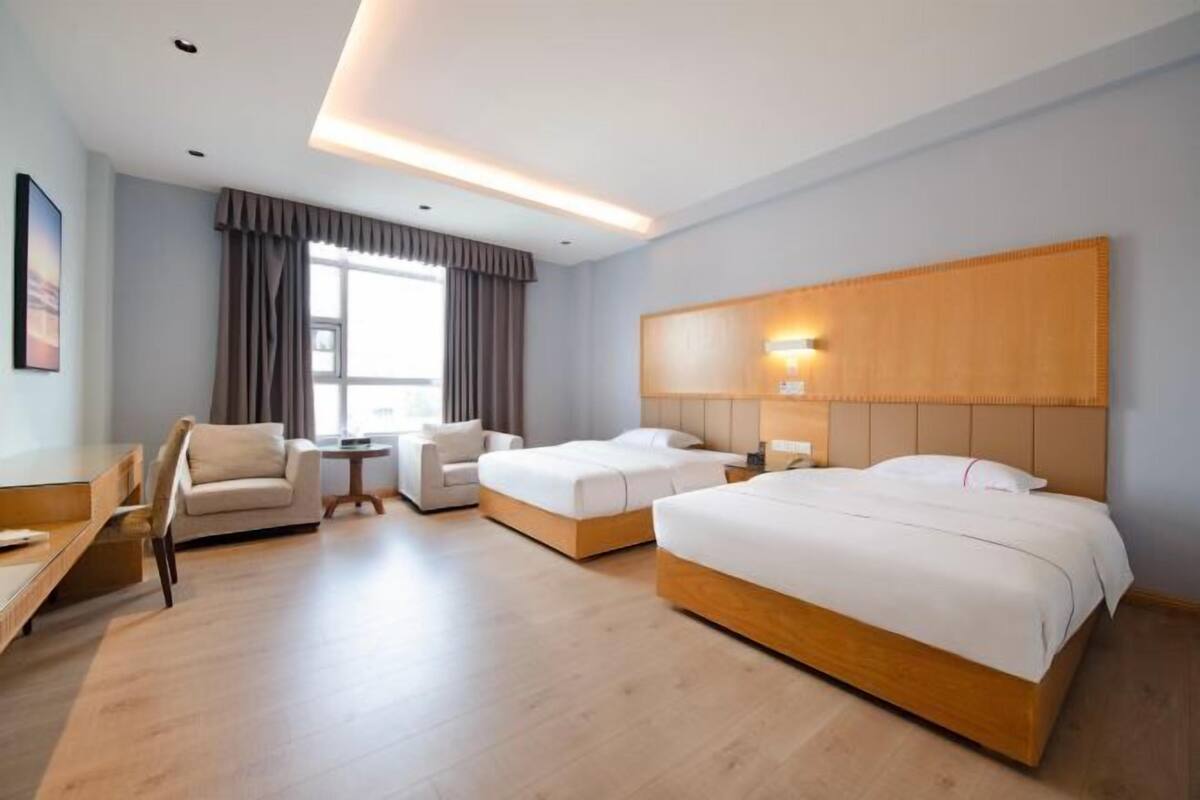Ein Hotelzimmer mit einem großen Bett, einem Einzelbett, einem Schreibtisch, einem Stuhl und einem fenster mit Vorhängen.