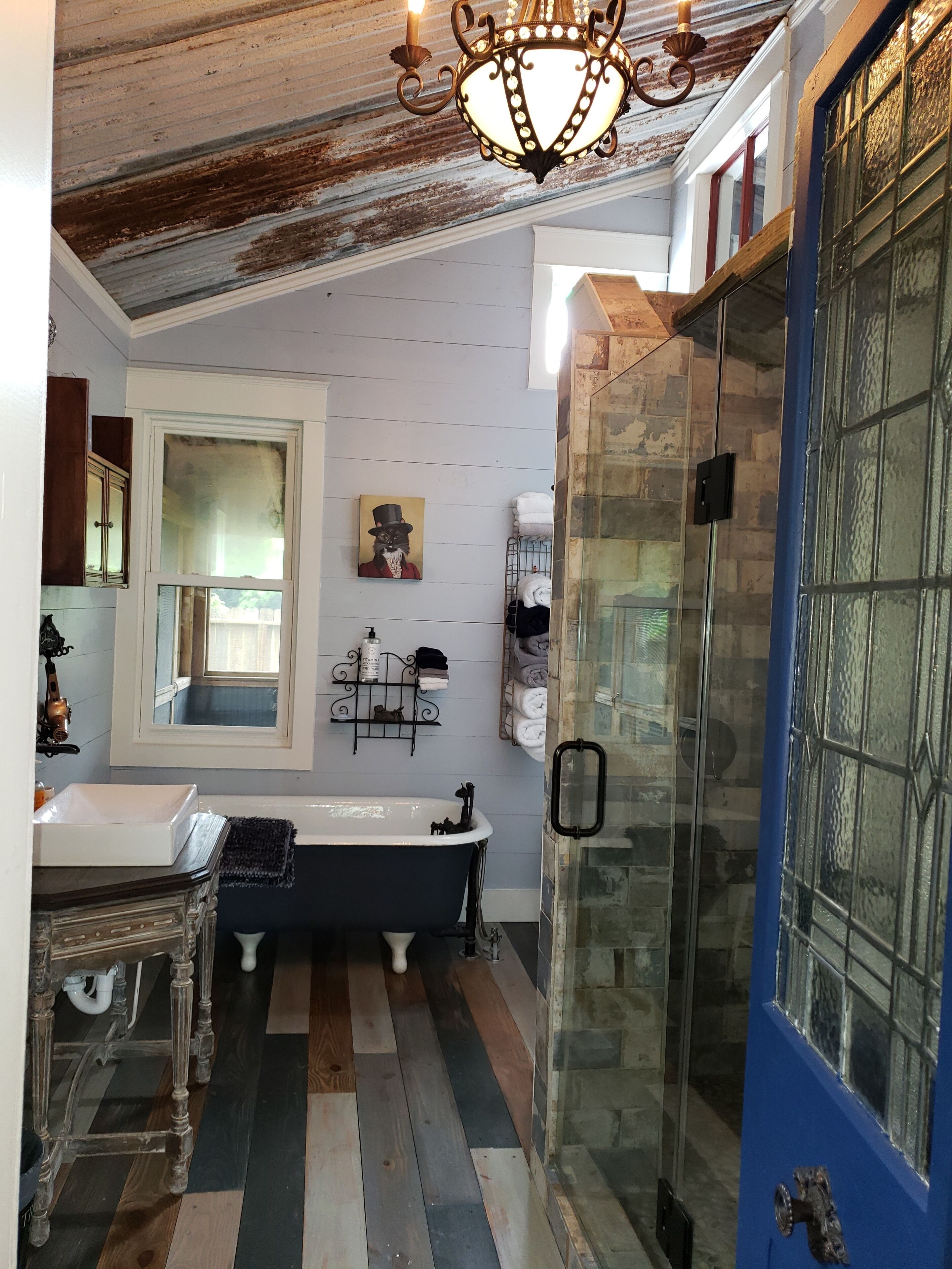A bathroom with a vintage bathtub, a glass shower enclosure, and a blue door.