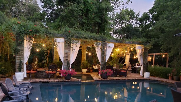 Zona junto a la piscina con sillas de descanso, una parrilla y un pérgola con luces colgantes.