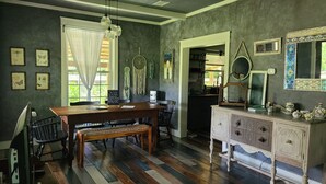 Un comedor con mesa de madera, sillas y banco. Hay un mostrador de buffet con una radio y adornos.