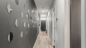 A hallway with a series of circular mirrors on the left wall, a wooden floor, and a door on the right. - Fishtown Haven 2 King Beds Gated Parking (Philadelphia)