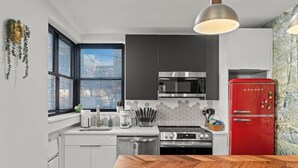 A modern kitchen with white cabinets, a red refrigerator, a microwave, and a wooden dining table. - Fishtown Haven 2 King Beds Gated Parking (Philadelphia)