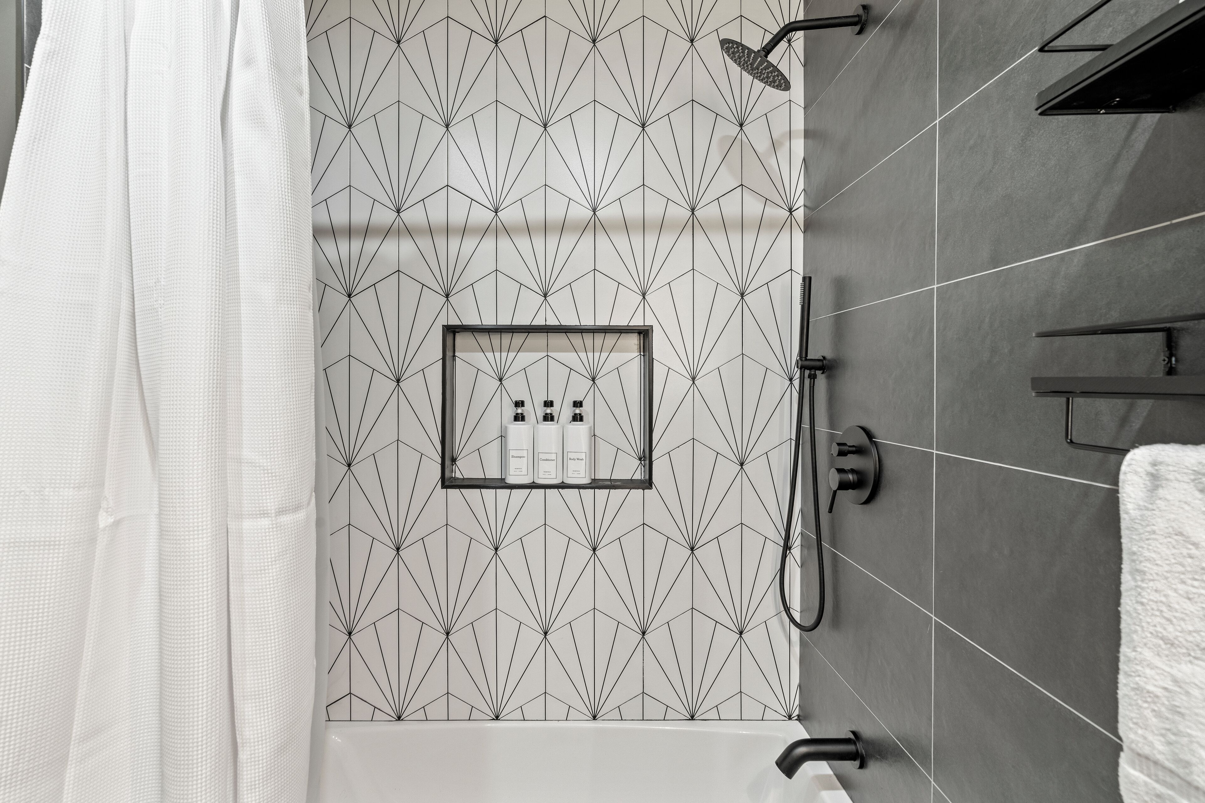 Un baño moderno con un revestimiento mural de diseño geométrico, zona de ducha y toallero.