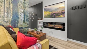 A modern living room with a large flat-screen TV, a fireplace, and a forest mural on the wall. - Fishtown Haven 2 King Beds Gated Parking (Philadelphia)