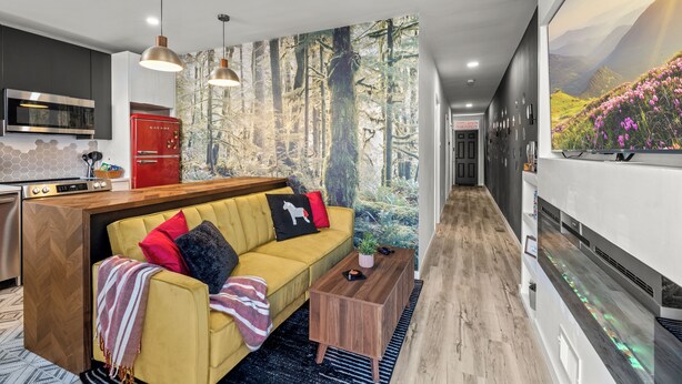 A modern living room with a yellow sofa, a red refrigerator, and a large wall mural of a forest. - Fishtown Haven 2 King Beds Gated Parking (Philadelphia)