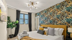 A neatly arranged bedroom with a bed, a potted plant, a window with curtains, and a patterned wall. - Fishtown Haven 2 King Beds Gated Parking (Philadelphia)