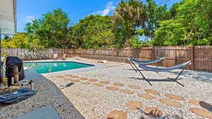 A backyard with a swimming pool, a hammock, and a grill.