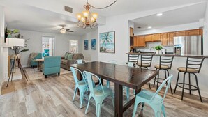 A spacious kitchen with wooden cabinets, a stainless steel refrigerator, and a dining area with a wooden table and turquoise chairs.