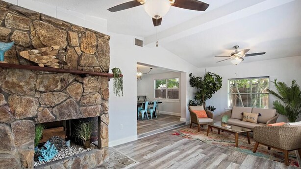 A spacious living area with a stone fireplace, wooden flooring, and a ceiling fan.