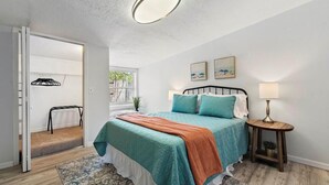 A bedroom with a bed, a bedside table with a lamp, a window with a view, and a door leading to another room.