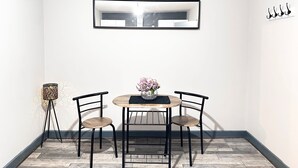 Ein Essbereich mit einem runden Tisch, zwei Stühlen, einer Blumenvase, einem Wandspiegel und einer Stehlampe.