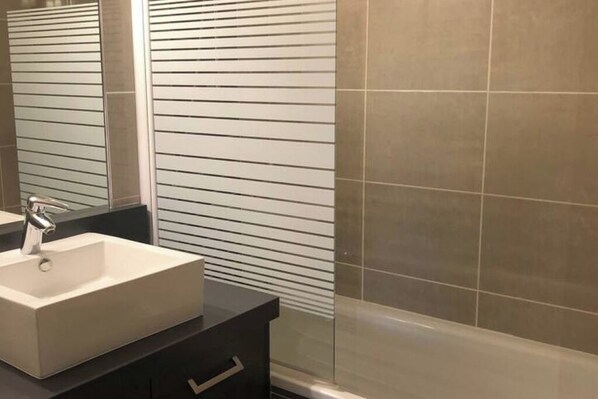 Un baño con un lavabo rectangular, un espejo y una pared con azulejos.