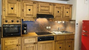 A kitchen with wooden cabinets, a microwave, a coffee maker, a dishwasher, and a red refrigerator.