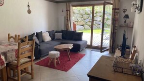 A cozy living room with a sofa, a dining table with chairs, a small stool, and a red rug.