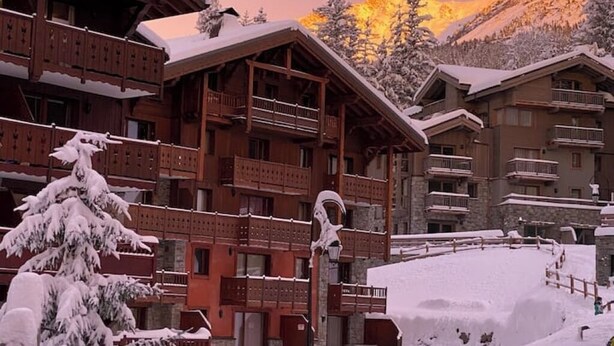 A wooden chalet-style building with balconies and a snow-covered landscape.
