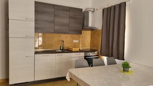 A compact kitchen with a dining area, featuring a stove, sink, and cabinets. - Apartments Radacic (Marina)