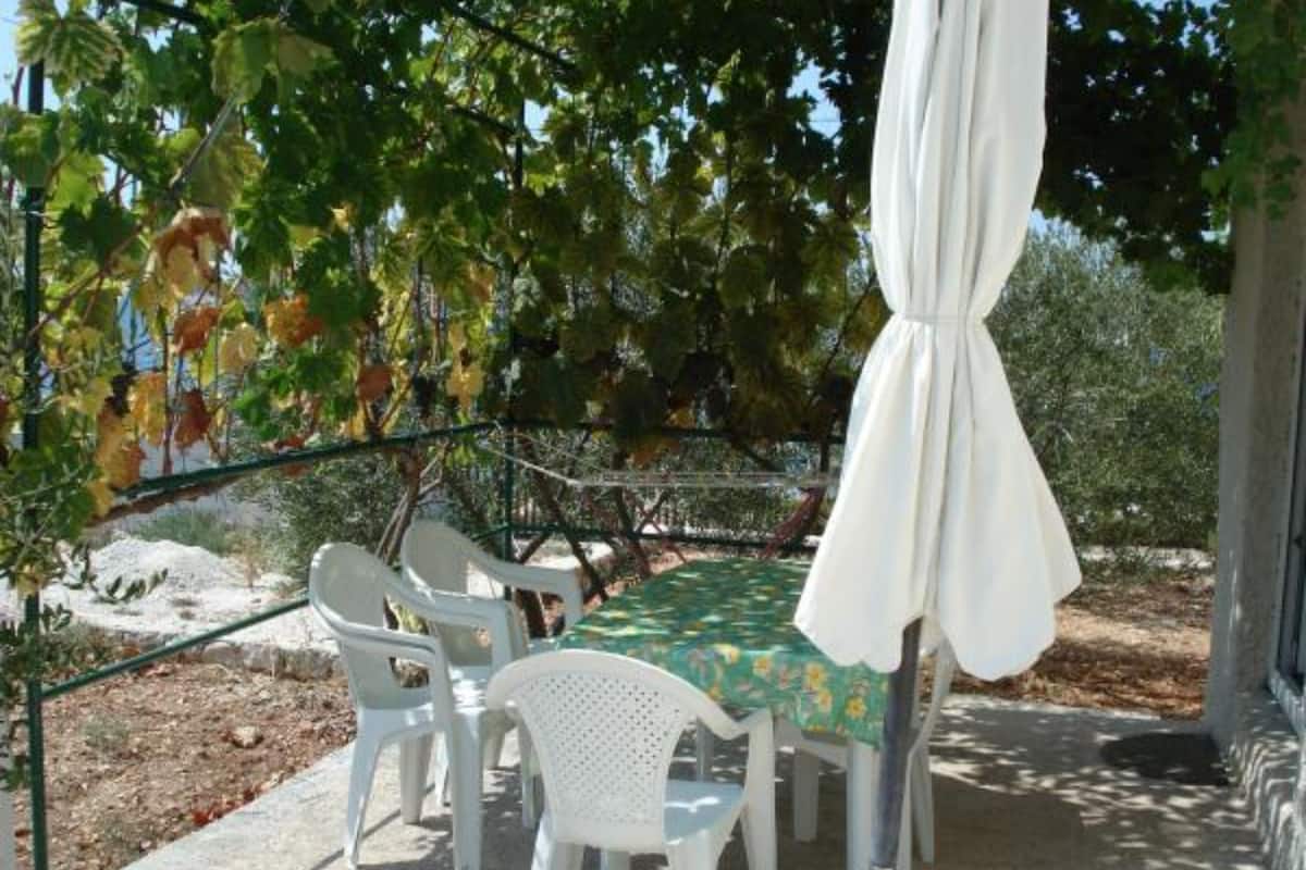 An outdoor patio with a table and chairs, surrounded by trees and a metal fence.